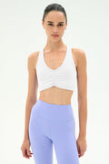 A woman models the SPLITS59 Airweight Bra with Ruching in white, paired with high-waisted pastel purple leggings, standing against a plain light background and looking directly at the camera.