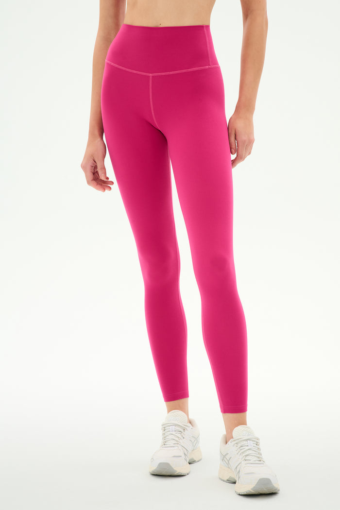 A person is wearing SPLITS59 Airweight High Waist Legging in Sangria, crafted from ultra-soft Airweight fabric, paired with white sneakers and standing against a plain white background—an ideal outfit for hot yoga or everyday comfort.
