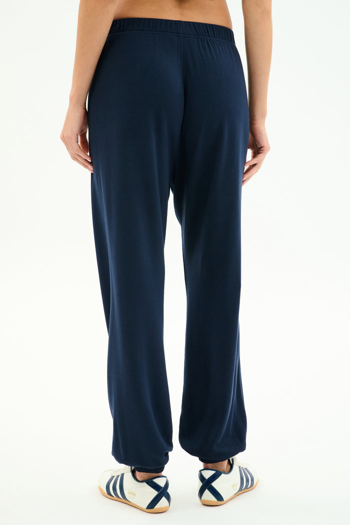 Model stands against a white background, shown from the back, wearing SPLITS59 Andie Oversized Fleece Varsity 59 Sweatpant in Indigo/59 and white sneakers with blue stripes. Made in Los Angeles.