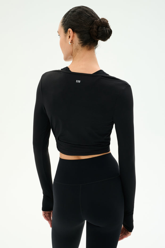 A woman wearing the SPLITS59 Bella Airweight Lite Wrap in black stands with her back to the camera against a plain light background.