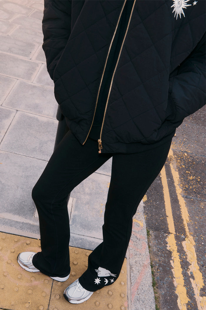 Black Cotton Wide Leg joggers with ecru embroidery motifs at the hem, styled with a quilted jacket for a London look.
