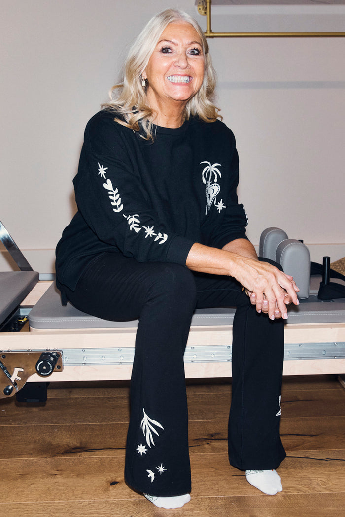 Black Cotton Wide Leg flares and sweatshirt with ecru embroidered motifs, worn by a woman on a Pilates reformer.