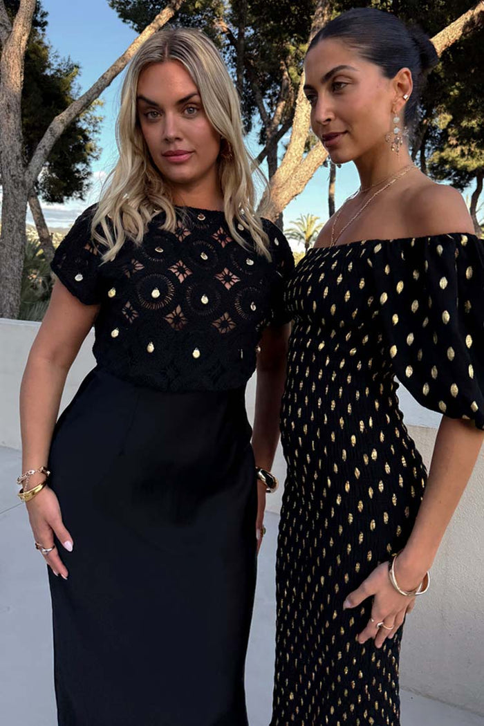 Black Crochet Shell Elodie Dress with gold shell crochet top and satin skirt, worn by a model in an outdoor setting.