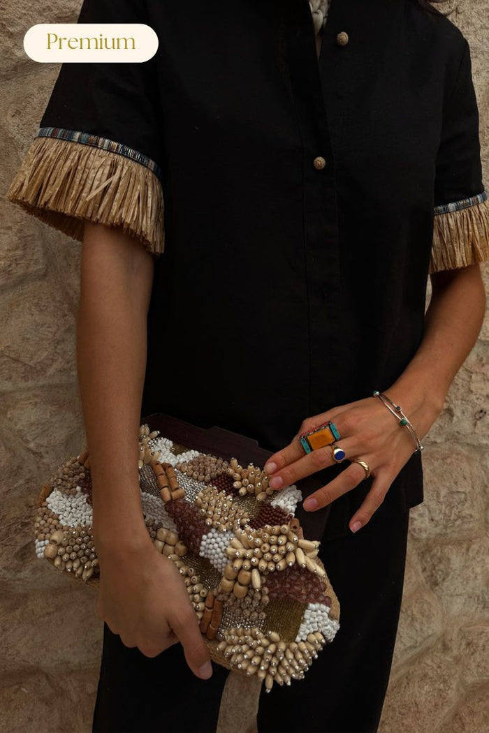 Black Raffia Shirt with fringe on the sleeves and crochet buttons, held alongside a beaded raffia clutch.