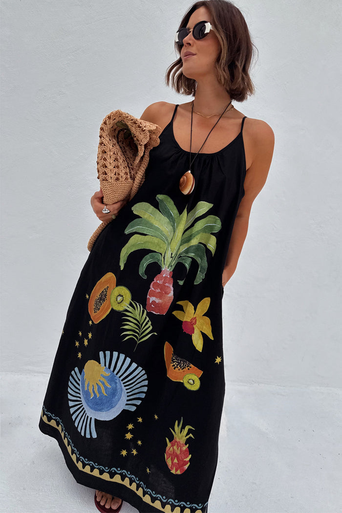 Black Rio Maxi Dress with hand-painted tropical fruit motifs, styled with a woven bag and sunglasses.