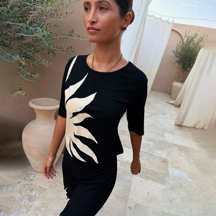 Black Sol Rib T-Shirt with a hand-painted sun print, styled in an outdoor Mediterranean courtyard.