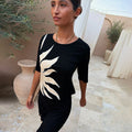 Black Sol Rib T-Shirt with a hand-painted sun print, styled in an outdoor Mediterranean courtyard.