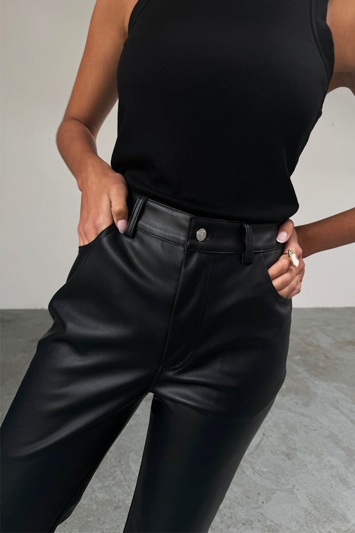 High-waisted Black Vegan Leather Trouser with front pockets, styled with a black ribbed tank top.