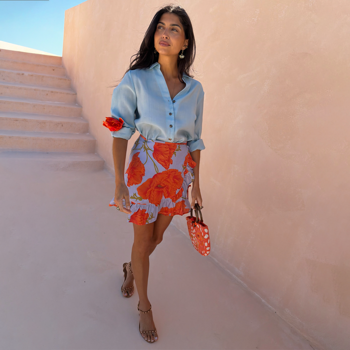Blue Poppy Mini Jaspre wrap skirt with a bold floral print and frill hem, styled with a light blue shirt.