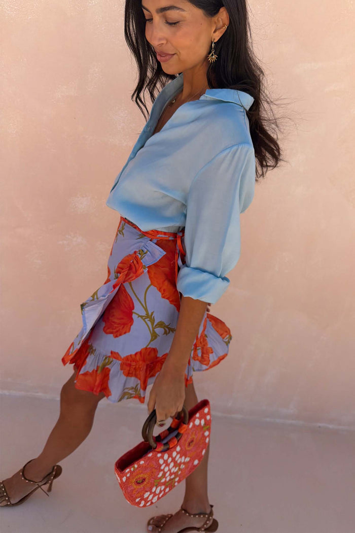 Blue Poppy Mini Jaspre wrap skirt with orange poppy print and frill hem, styled with a light blue shirt.