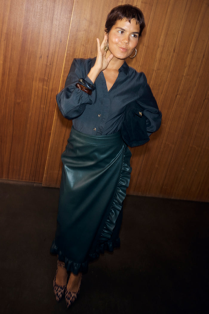 Bottle green vegan leather wrap Jaspre skirt featuring ruffle detailing, styled with a navy shirt and leopard heels.