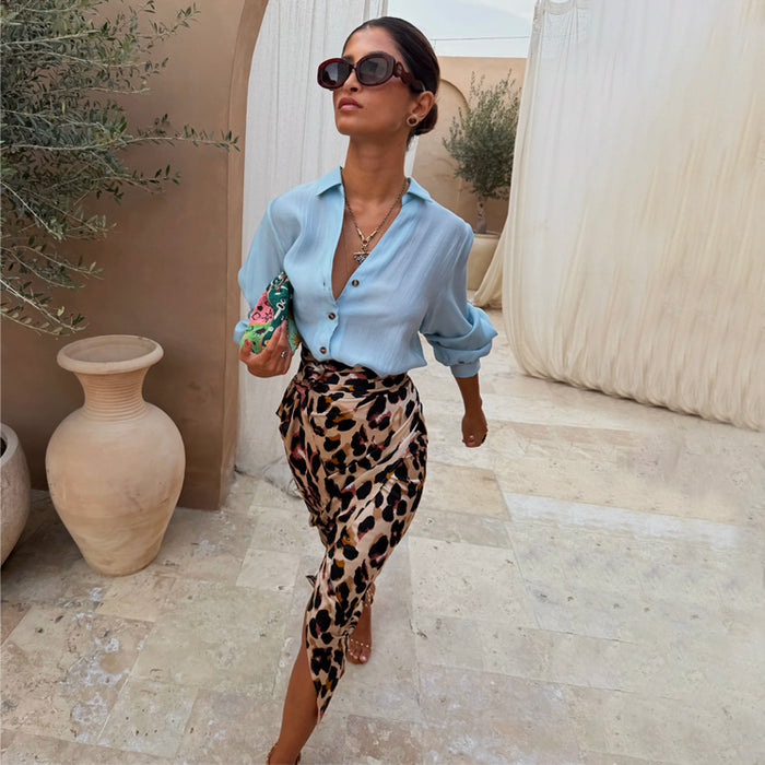 Iconic Brown Leopard Jaspre Skirt in satin, styled with a light blue shirt and sunglasses in an outdoor setting.