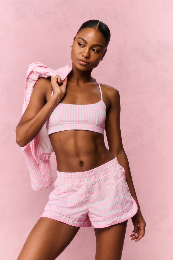 Woman wearing a pink gingham sports bra and shorts outfit against a pink background