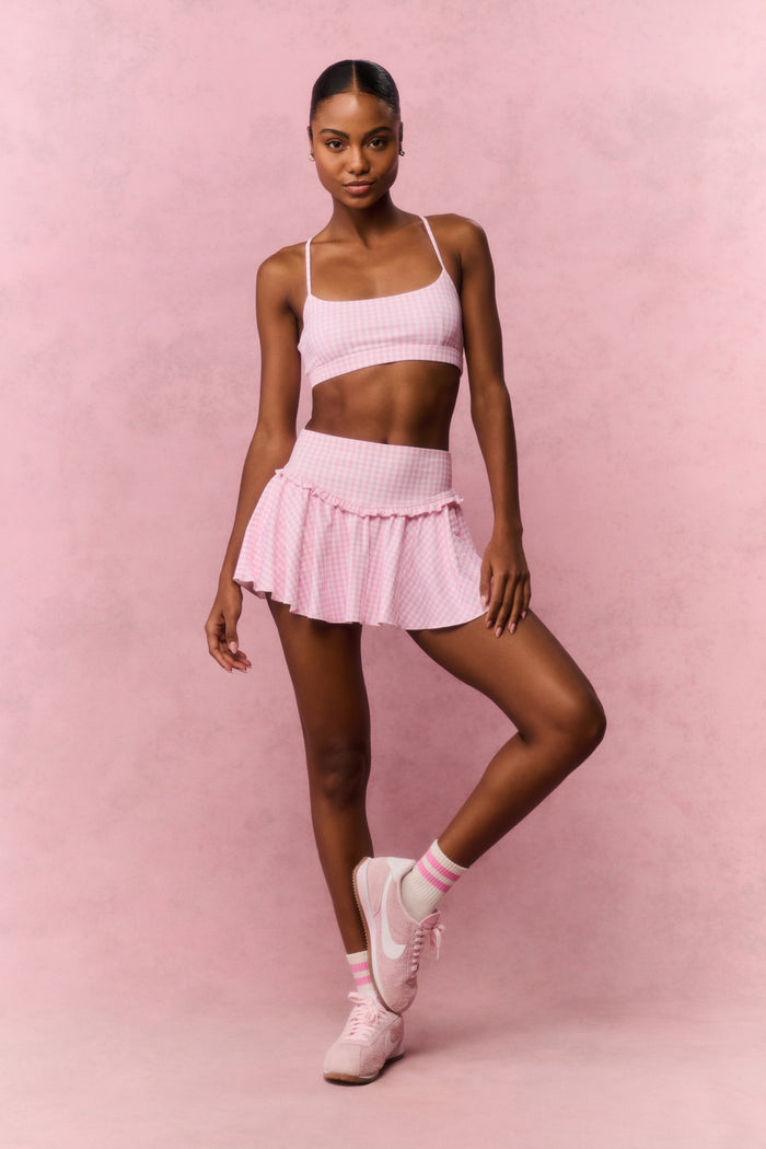 Woman wearing a pink gingham sports bra and skirt outfit against a pink background