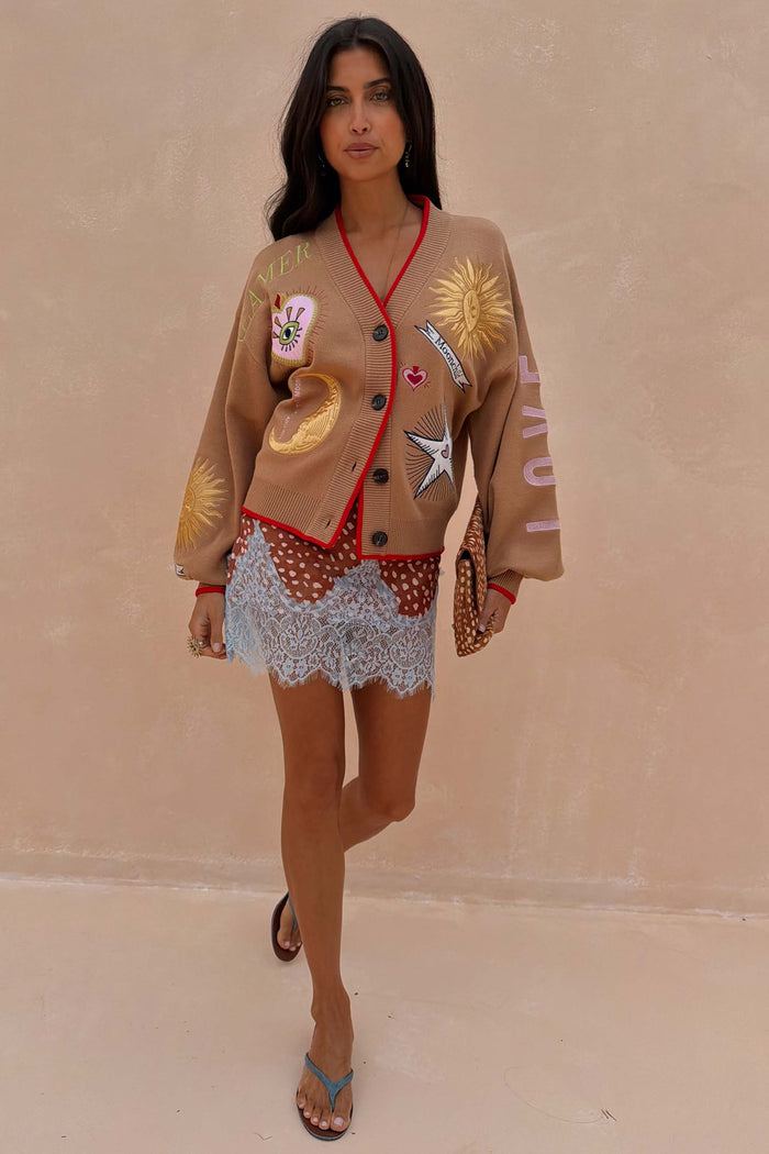 Camel Mystical Cardigan with celestial embroidery and red trim worn over a patterned blue lace dress.