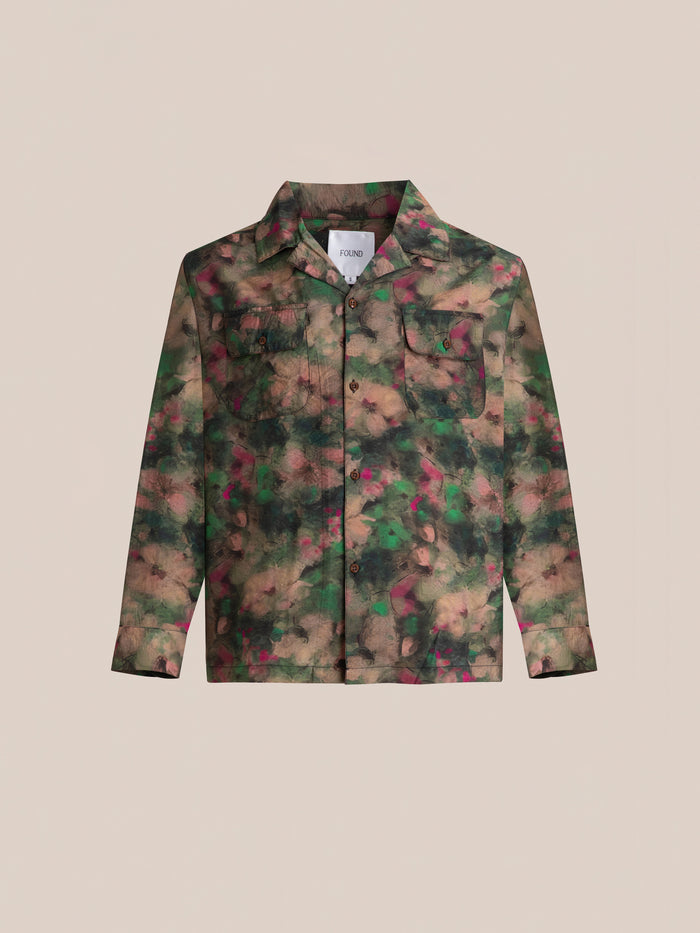 Introducing the Charlot LS Camp Shirt by FOUND, a stylish button-up with a camouflage pattern in shades of green, brown, and pink. This shirt features dual chest pockets and is displayed on a beige background.