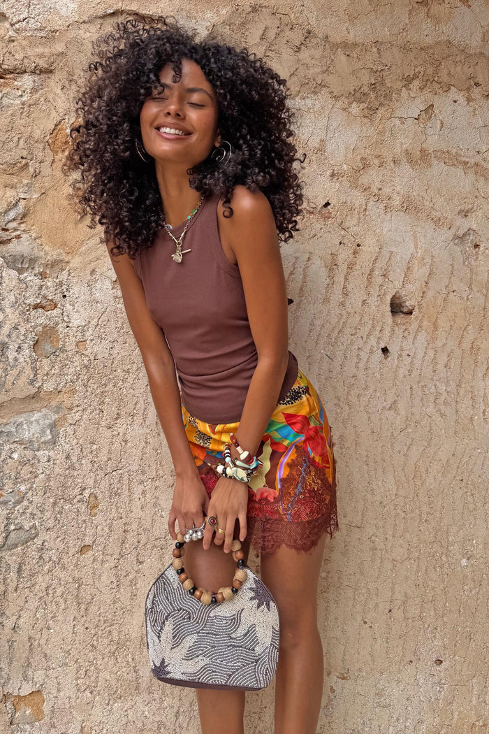 Chocolate Ribbed Tank styled with a colourful floral skirt and beaded bag against a stone wall.