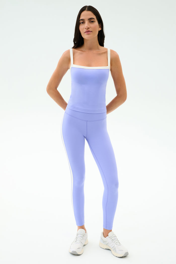 A person faces forward in SPLITS59 Clare High Waist Rigor 7/8 leggings in Purple Haze/White, paired with white sneakers, ready for the gym against a plain light background.
