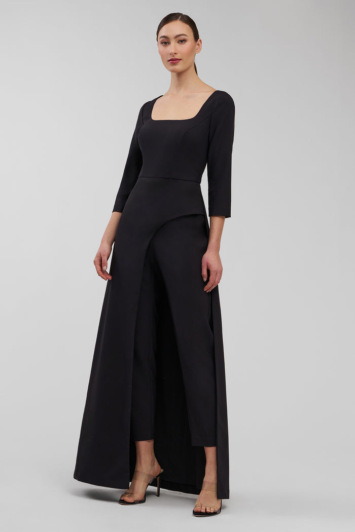 Woman wearing a black walk thru jumpsuit with a plain background