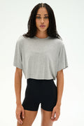 A woman stands facing forward against a plain white background, wearing the SPLITS59 Djuna Oversized Crop Jersey Tee in Heather Grey and high-waisted black shorts.