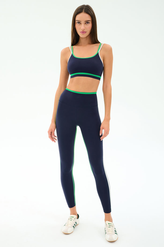 A woman faces forward wearing the SPLITS59 Eva Rigor Double Strap Bra in Indigo/Spearmint, paired with matching high-waisted leggings and white sneakers, set against a plain light background.