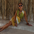 Green Ombre Deia Mini Dress in earthy green and yellow with raffia edge trim, styled for a beach holiday.
