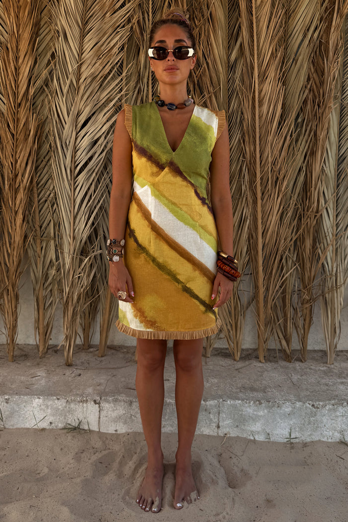 Green Ombre Deia Dress with yellow tones and raffia trim, styled for a vacation against palm leaves.