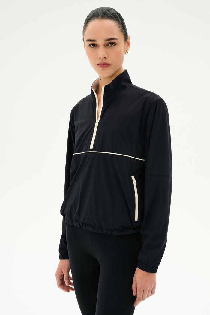 A woman wears the SPLITS59 Lyle Woven Nylon Pullover in Black/Creme with matching black spandex pants, standing against a plain white background.