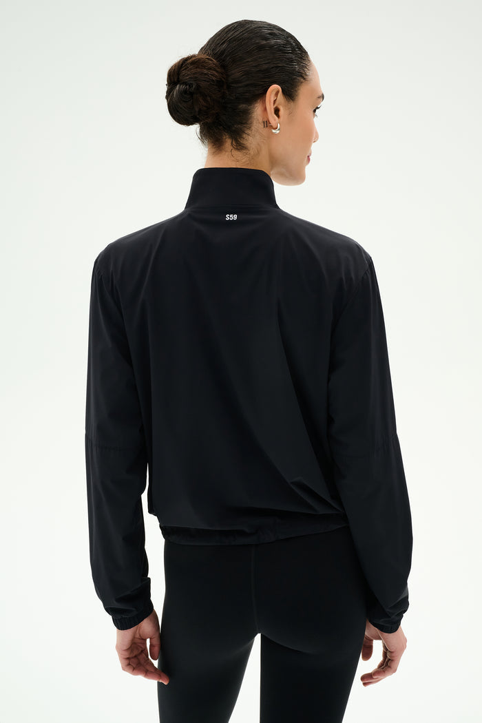 A person with dark hair in a bun is shown from the back against a plain light background, wearing the SPLITS59 Lyle Woven Nylon Pullover in Black/Creme.