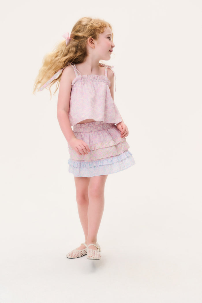 Young girl in a light pink skirt and matching sleeveless top with ruffled layers on a white background