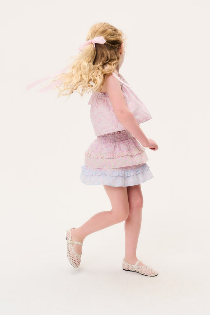 Young girl in a light pink skirt and matching sleeveless top with ruffled layers on a white background