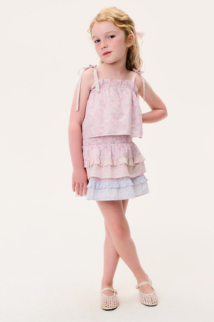 Young girl wearing a pink sleeveless top and matching skirt with ruffled layers on a white background