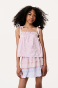 Young girl wearing a light pink top and white skirt with ruffled layers on a plain background