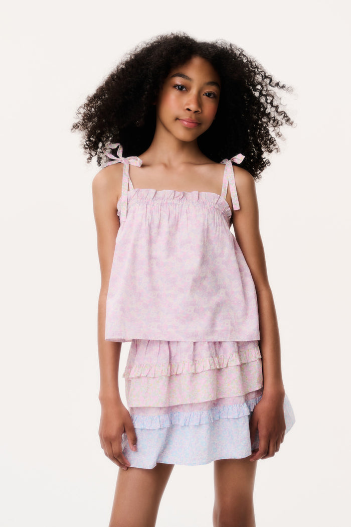 Young girl wearing a light pink top and white skirt with ruffled layers on a plain background