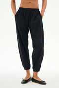 Model wears the SPLITS59 Megan Woven Nylon Jogger in black, featuring a cinched waistband and hands in pockets, paired with black ballet flats. Shown from chest down against a plain background.