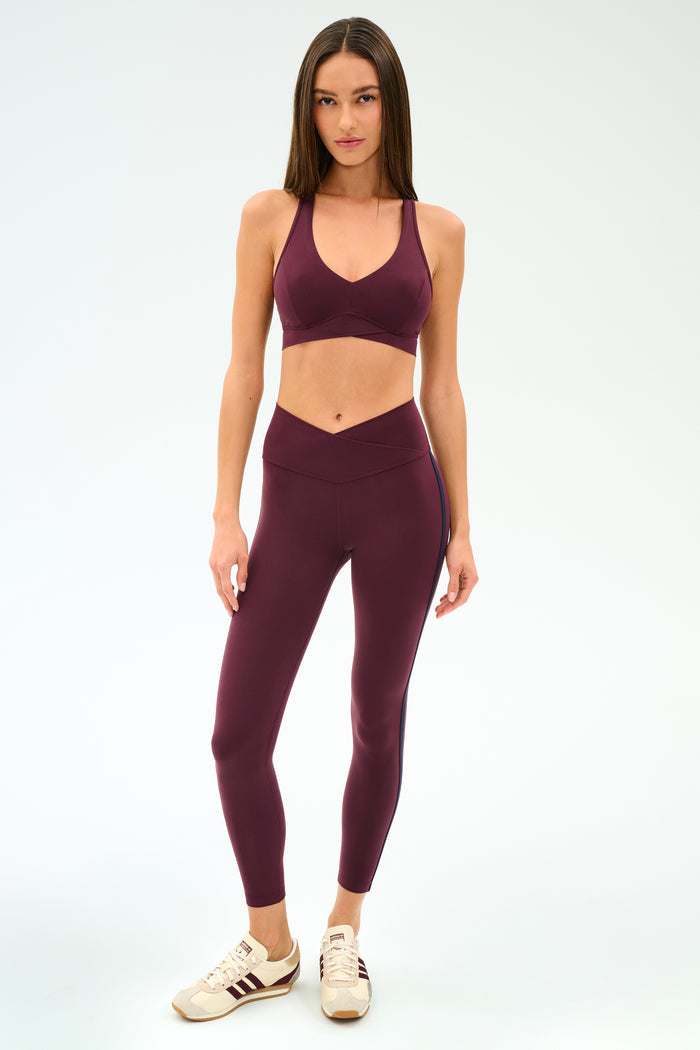 Woman wearing the SPLITS59 Mia Rigor Bra in Dark Cherry with matching leggings and beige sneakers, standing against a plain light background.