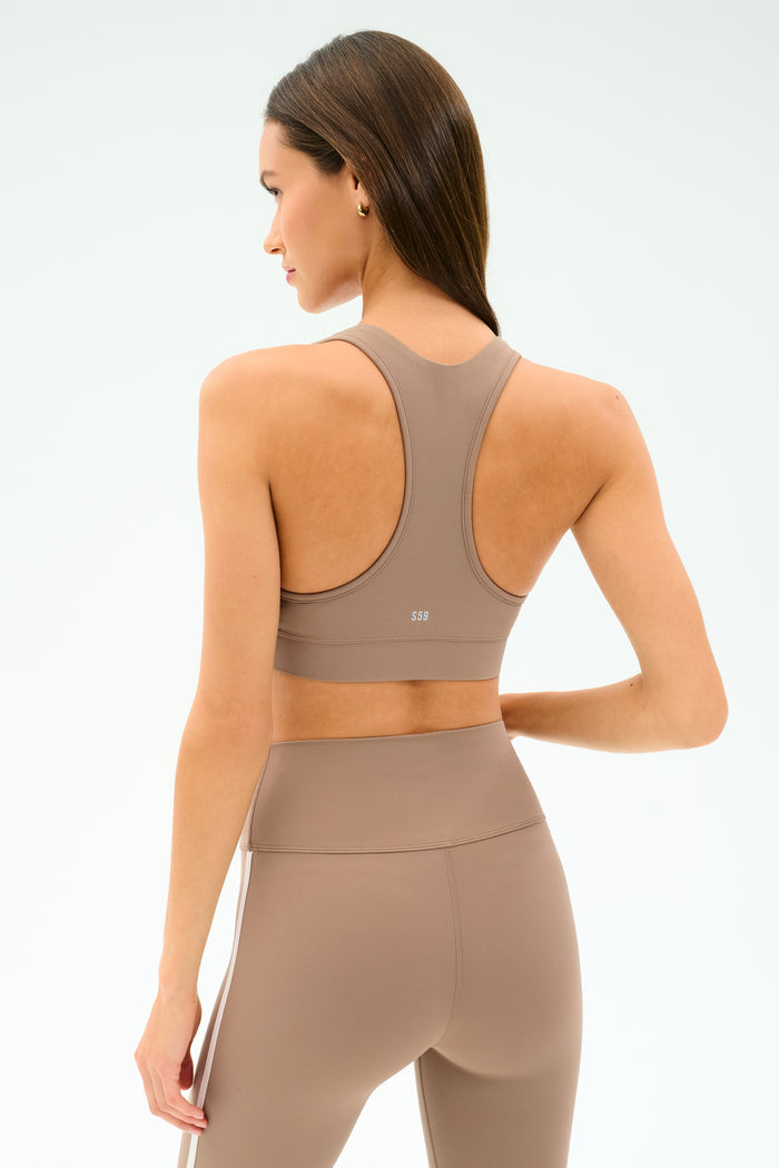 A woman faces away from the camera, wearing the SPLITS59 Mia Rigor Bra in Latte with matching high-waisted leggings, set against a plain light background.