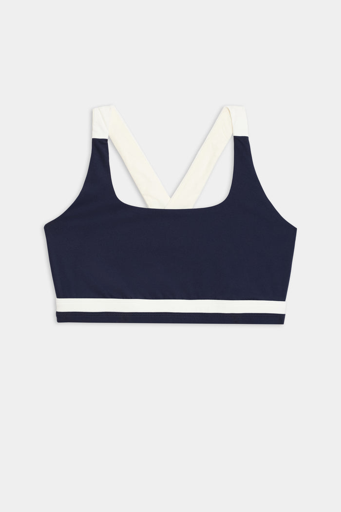 The Miles Rigor Bra by SPLITS59, featuring a navy design with wide white straps and a white band under the bust, is displayed on a light gray background.