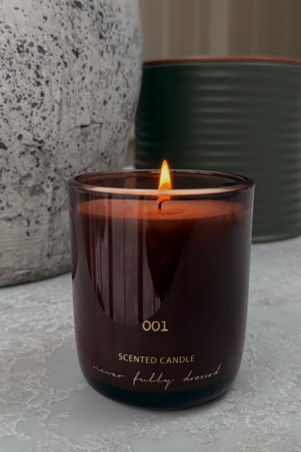 Lit NFD Eau De Parfum Candle 001 in a dark burgundy glass vessel with gold lettering and a flickering flame.