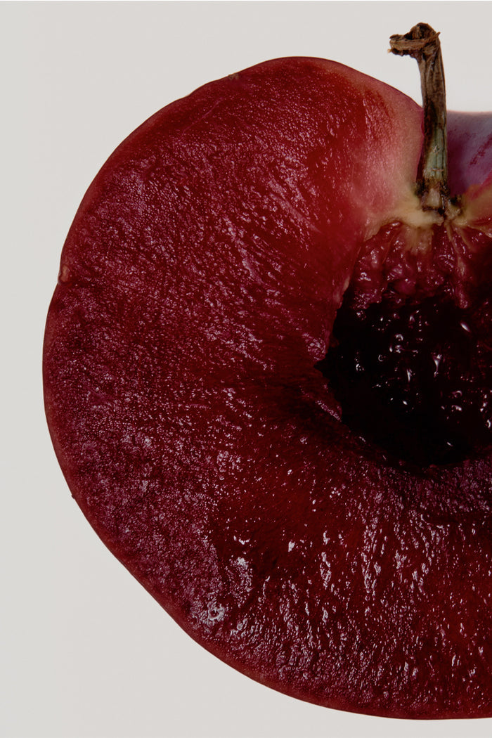 Deep red sliced plum with a dark stone, highlighting a key fragrance note for the NFD Candle 001.