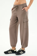 A person wears SPLITS59’s Nico Airweight Cargo Pant in Lentil, featuring a drawstring waist and side pockets, paired with black athletic shoes against a white background—ideal for workouts or casual outings.