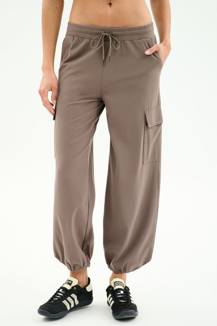 Wearing SPLITS59 Nico Airweight Cargo Pant in Lentil with side pockets and drawstring waist, paired with black sneakers—ideal for lightweight comfort during workouts, shown against a white background.