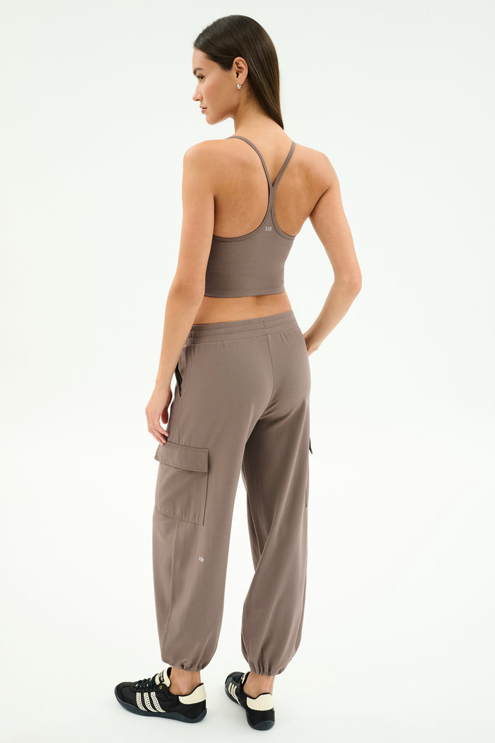 A woman faces away, wearing SPLITS59's Nico Airweight Cargo Pant in Lentil and a taupe sports bra with black Adidas sneakers against a white background—an ideal look for your next workout.