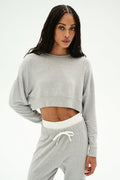 A woman wears the SPLITS59 Noah Fleece Crop Sweatshirt in Heather Grey, featuring a soft modal-spandex blend and matching sweatpants with a white waistband, standing against a plain light background.