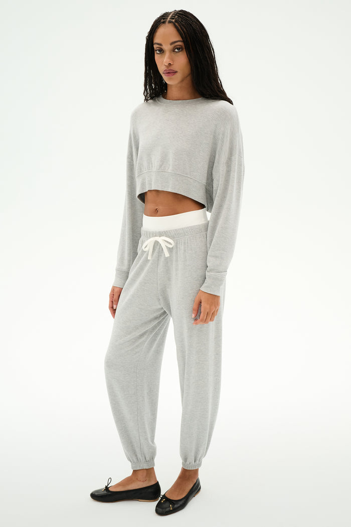 A woman wears the SPLITS59 Noah Fleece Crop Sweatshirt in Heather Grey with matching sweatpants and black flats, standing against a plain white background.