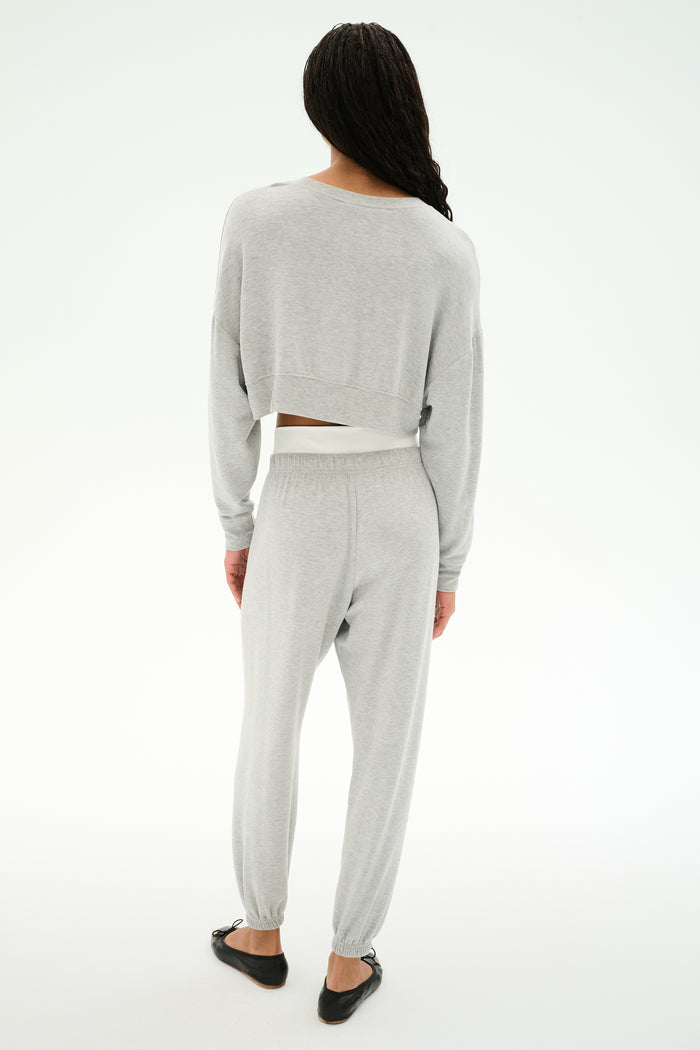 A person stands with their back to the camera, wearing the SPLITS59 Noah Fleece Crop Sweatshirt in Heather Grey, paired with matching sweatpants and black flat shoes against a plain white background.