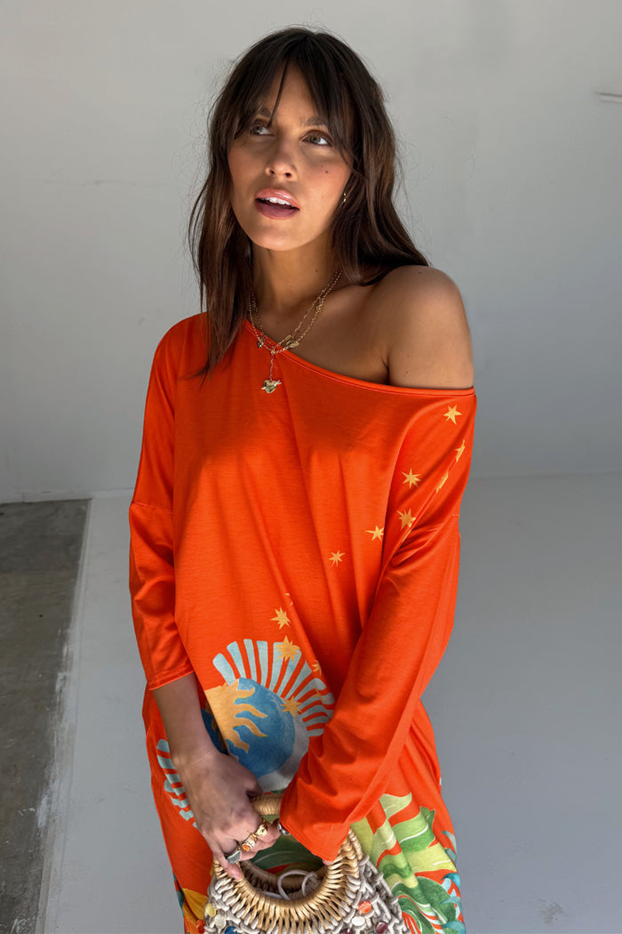 Orange Rio Jem Dress in a relaxed one-shoulder silhouette with a sun and star print, styled with a straw bag.