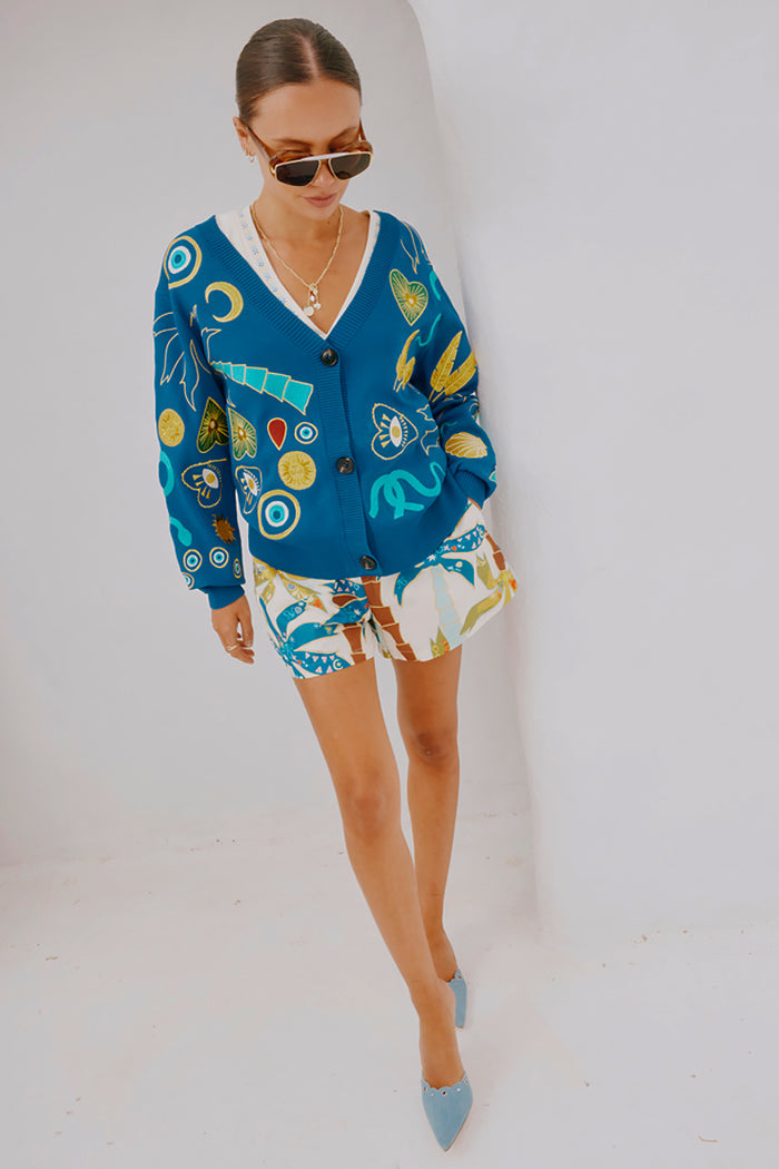 Palm Elissa Shorts in a cotton-linen multi-colour palm print, styled with a blue motif cardigan and heels.