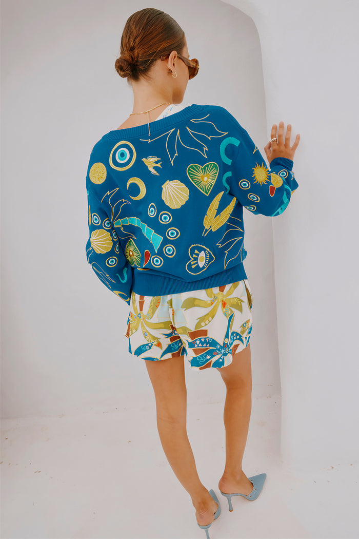 Palm Elissa Shorts in a multi-coloured palm leaf print, styled with a blue motif jumper and heels.