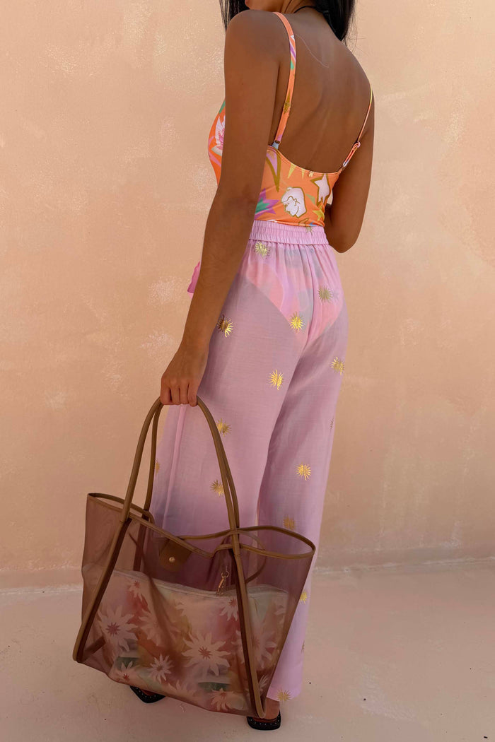 Pink Elissa Trousers with gold foil sun motifs and a wide-leg fit, paired with a printed swimsuit and mesh bag.